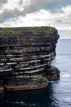 Dramatic stratified rock formations on the coast, green clifftop over the deep b Fotos Stock