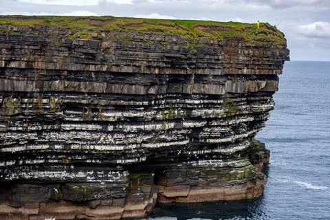 Dramatic stratified rock formations on the coast, green clifftop over the deep b Fotos Stock