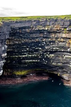 Dramatic stratified rock formations on the coast, green clifftop over the deep b Fotos Stock