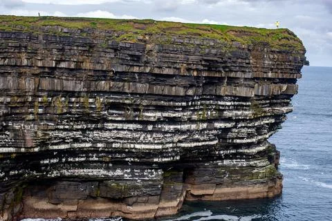 Dramatic stratified rock formations on the coast, green clifftop over the deep b Fotos Stock