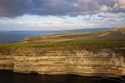 Dramatic stratified rock formations on the coast, green clifftop over the deep b Fotos Stock