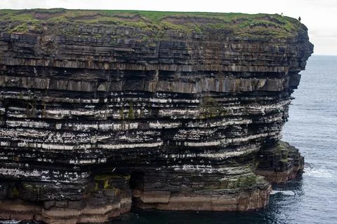 Dramatic stratified rock formations on the coast, green clifftop over the deep b Fotos Stock