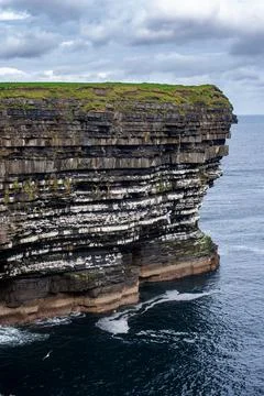 Dramatic stratified rock formations on the coast, green clifftop over the deep b Fotos Stock