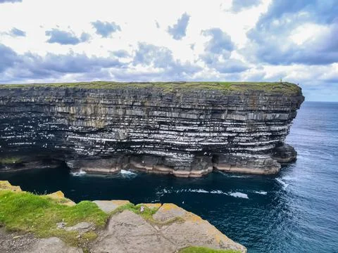 Dramatic stratified rock formations on the coast, green clifftop over the deep b Fotos Stock