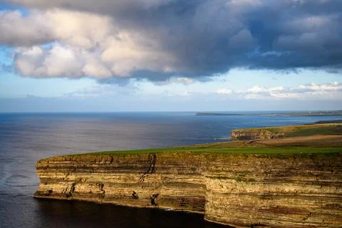 Dramatic stratified rock formations on the coast, green clifftop over the deep b Fotos Stock
