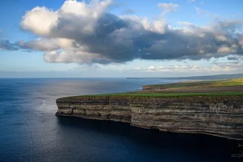 Dramatic stratified rock formations on the coast, green clifftop over the deep b Fotos Stock