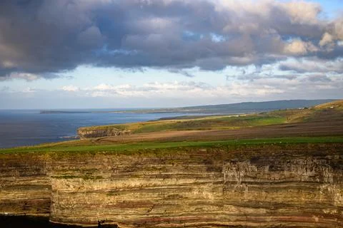 Dramatic stratified rock formations on the coast, green clifftop over the deep b Fotos Stock