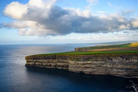 Dramatic stratified rock formations on the coast, green clifftop over the deep b Fotos Stock