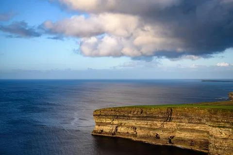 Dramatic stratified rock formations on the coast, green clifftop over the deep b Fotos Stock
