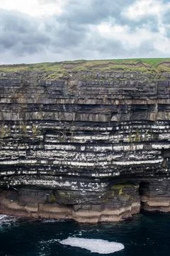 Dramatic stratified rock formations on the coast, green clifftop over the deep b Fotos Stock