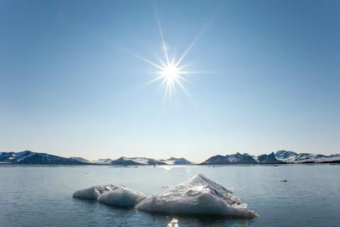 A dramatic sun burst over arctic mountains and a floating iceberg  Stock Photos
