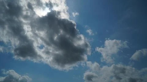 Dramatic Sun Peeking Above Dark Cloud in Blue Sky with Scattered Clouds Stock Photos