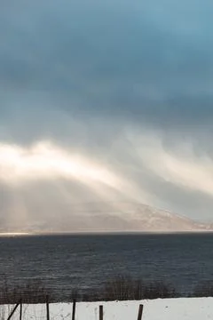 Dramatic sun rays break through storm clouds over a dark fjord in Northern .. Stock Photos