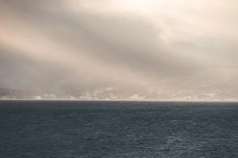 Dramatic sun rays break through storm clouds over a dark fjord in Northern .. Stock Photos