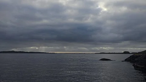 Dramatic sun rays breaking through heavy clouds over Norwegian sea and hills Stock-Footage 345168145