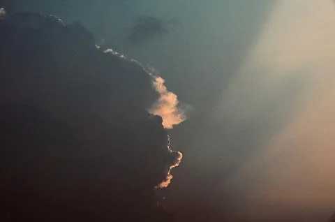 Dramatic sun rays breaking through heavy storm clouds at sunset Stock Photos