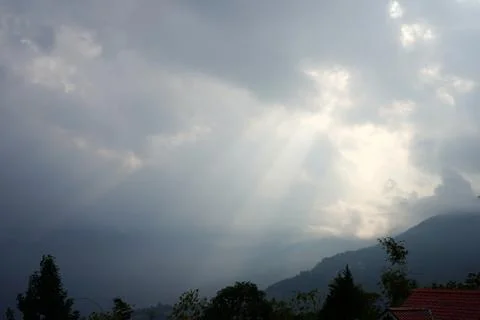 Dramatic sun rays piercing through dark storm clouds over mountain landscape Stock Photos