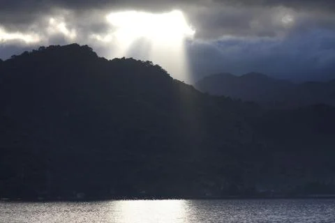 Dramatic sun rays shining through stormy clouds over tranquil mountains Stock Photos