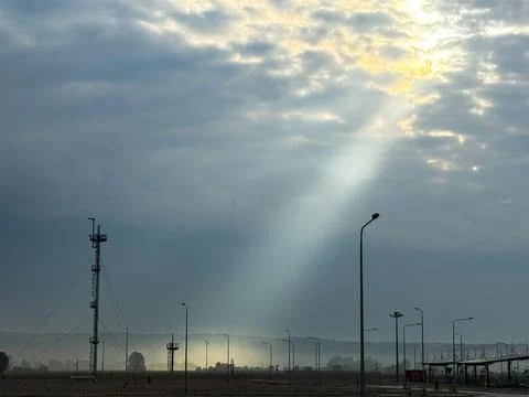 A dramatic sunbeam breaks through cloudy skies over an industrial landscape Stock Photos