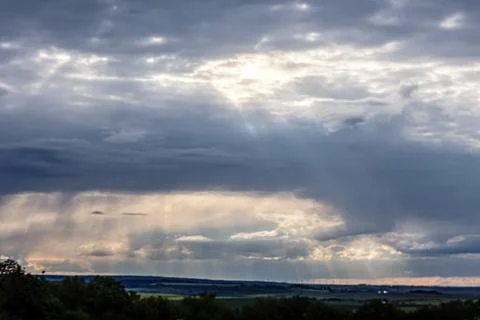 Dramatic sunbeams break through stormy clouds over a rural landscape 스톡 사진