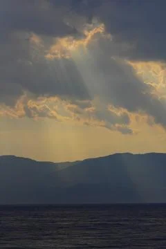 Dramatic sunbeams breaking through clouds over mountains. Stock Photos