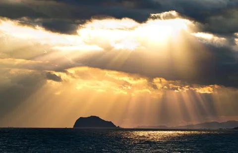 Dramatic Sunbeams Breaking Through Storm Clouds Over a Remote Island at Sea. Stock Photos