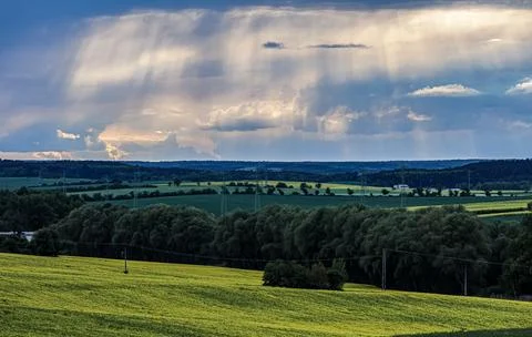 Dramatic sunbeams pierce stormy clouds over a vibrant yellow field Foto stock