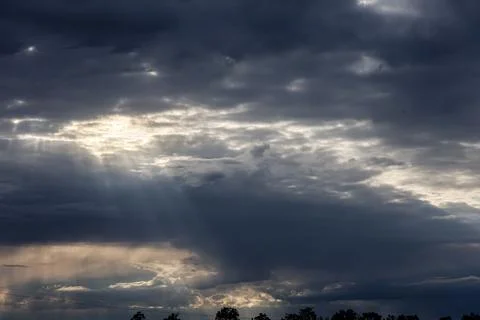 Dramatic sunbeams pierce through dark, stormy clouds at sunset Foto stock