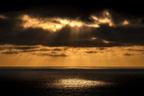 Dramatic sunbeams pierce through dark clouds over a shimmering ocean horizon Fotos de archivo