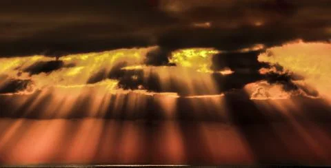 Dramatic sunbeams pierce through dark clouds over the ocean at sunset 스톡 사진