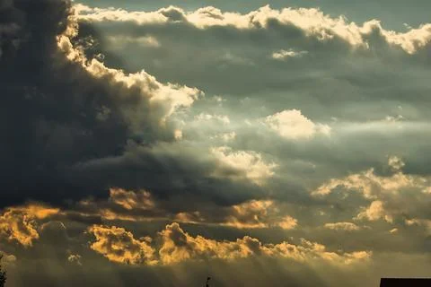 Dramatic sunbeams pierce through dark storm clouds at sunset Stock Photos