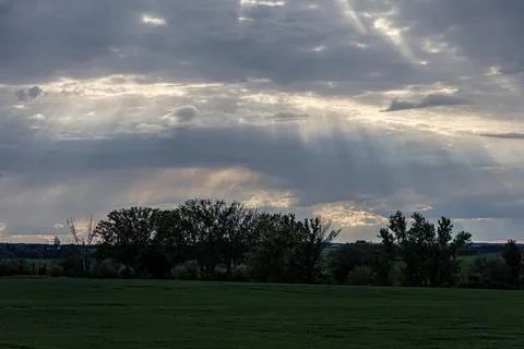 Dramatic sunbeams pierce through stormy clouds over a green landscape 写真素材