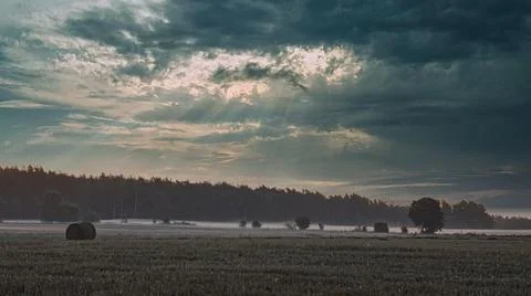 Dramatic sunbeams pierce through stormy clouds over a misty rural landscape Fotos Stock
