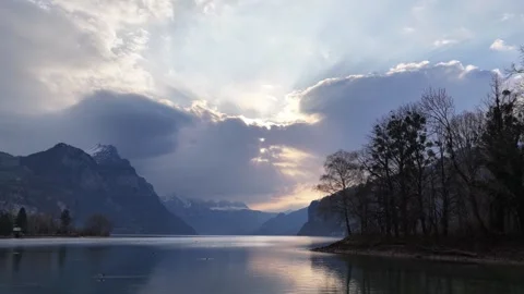 Dramatic Sunlight and Clouds Over Mountain Lake With Bare Trees and Reflections Video stock 337788082