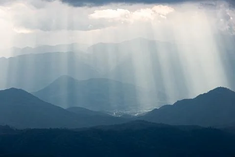 Dramatic sunlight from cloudy sky shining to dark blue mountain range. Stock Photos