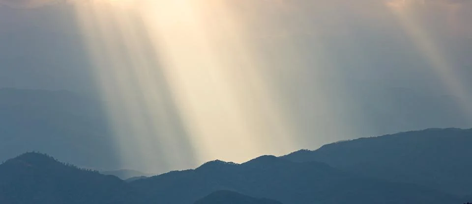 Dramatic sunlight shining onto blue mountain range. Stock Photos