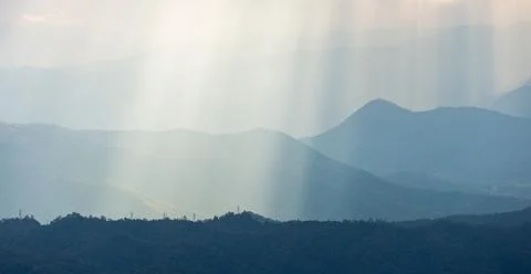 Dramatic sunlight shining onto blue mountain range. Stock Photos