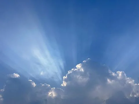 Dramatic sunlight streams through towering clouds in a bright blue sky Stock Photos