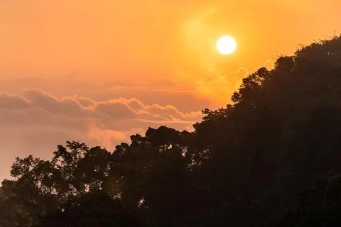 Dramatic sunrise and cloudy orange sky over silhouetted mountain. Stock Photos