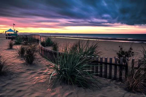 Dramatic sunrise on the beach with clouds, grass and wooden fence 스톡 사진