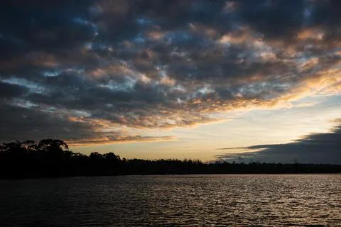 Dramatic sunrise sky covered by clouds make darkness to the water and land. Stock Photos