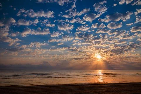 Dramatic sunrise sky with sunbeams breaking through light clouds over a sea Stock Photos