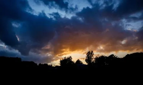 Dramatic sunset against mountains with trees and clouds Stock Photos
