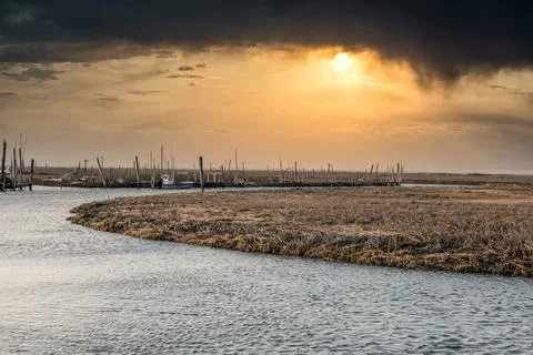 Dramatic sunset with black clouds on a river with a pier and boats 库存照片