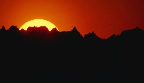 Dramatic sunset with a brilliant yellow sun sinking behind a rugged black m.. Stock Photos