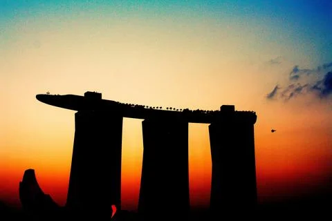 Dramatic sunset casts shadow of iconic Merlion statue on still harbor Foto stock