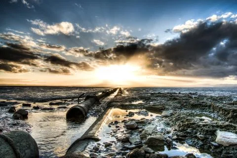 Dramatic sunset with clouds on the beach and a pipe that goes to the horizon. Stock-Fotos