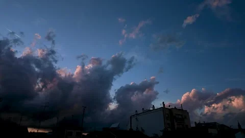 Dramatic sunset clouds glowing above urban rooftops against a darkening eve.. Video stock 344808952