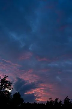 Dramatic sunset clouds glowing with pink light in dark blue evening sky Stock Photos