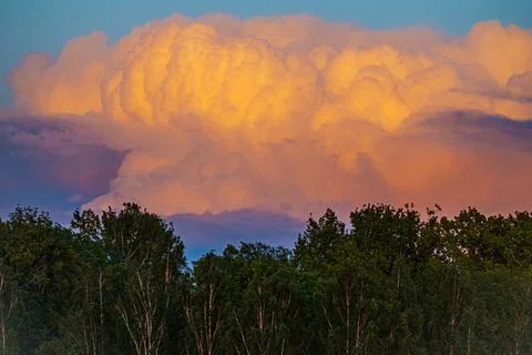 Dramatic sunset clouds illuminated in orange and yellow hues above a dense .. 스톡 사진